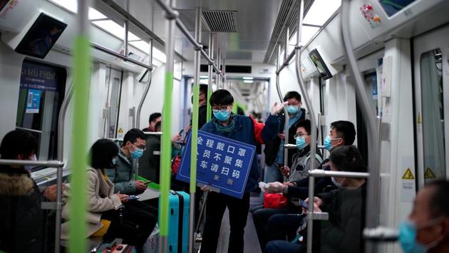 A staff member wearing a face mask holds a placard while standing among passengers on a subway train, on the first day the city's subway services resumed. The Chinese characters on the placard read: “Wear a mask for the entire journey, people should not gather and when you disembark please scan the health code.” (Aly Song / REUTERS)