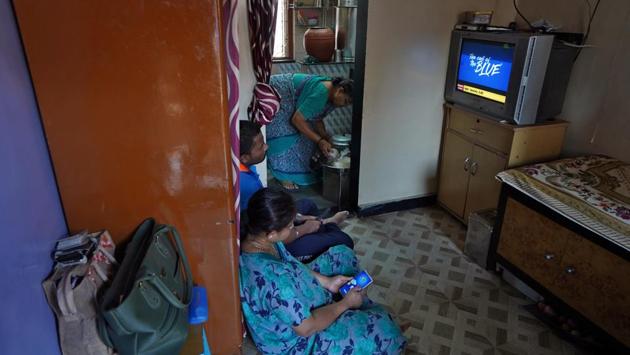 Suvarna Dinesh Rasal, a nurse at Breach Candy Hospital Trust watches TV with her son Atharva, who works at a coffee shop. Aparna Arvind Lanjekar, Suvarna’s mother, prepares food as they stay indoors inside their single room apartment at a chawl, home to hundreds of families, in Mumbai. (Hemanshi Kamani / REUTERS)