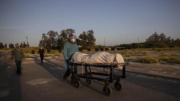 A member of Hevra Kadisha, an organization which prepares bodies of deceased Jews for burial according to Jewish tradition, pushes a body during a funeral of a Jewish man who died from coronavirus in the costal city of Ashkelon, Israel.(AP) A member of Hevra Kadisha, an organization which prepares bodies of deceased Jews for burial according to Jewish tradition, pushes a body during a funeral of a Jewish man who died from coronavirus in the costal city of Ashkelon, Israel.(AP)