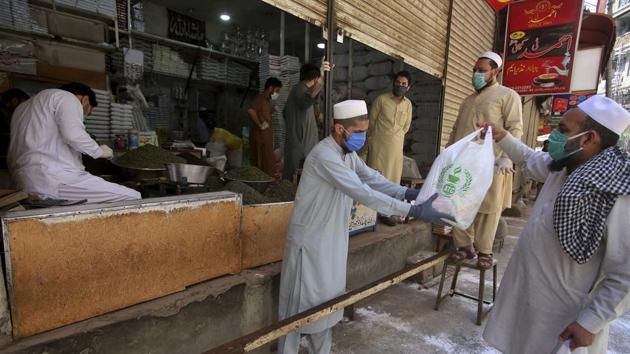 A shopkeeper deals customers with distance to help avoid the spread of coronavirus, in Peshawar, Pakistan, on Saturday.(AP Photo)