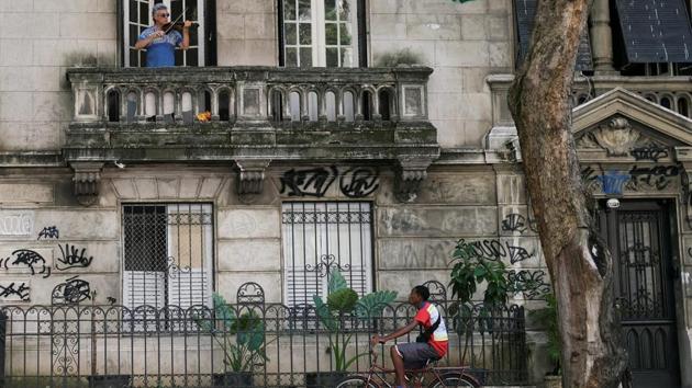 Adelmo Carvalho, 55, a sales representative who used to play in the church, plays the violin on his balcony as a deliveryman rides past in Rio de Janeiro, Brazil. (Rocardo Moraes / REUTERS)