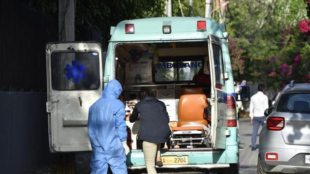 A health worker in a Personal Protective Equipment (PPE) suit helps a person who tested positive for Covid-19 into an ambulance, on day thirteen of the 21-day nationwide lockdown to curb the spread of coronavirus at Sainik Farms.(Sanjeev Verma/ Hindustan Times)