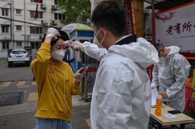 A man wearing a protective suit checks a woman's temperature next to a residential area in Wuhan, in China's central Hubei province on April 7, 2020.(AFP)