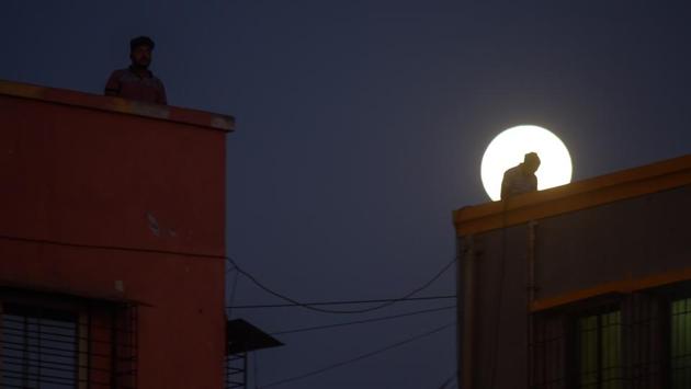 People on their terraces pictured against the rising moon during India’s 21-day lockdown against the coronavirus in Mumbai’s Versova area. (Ragul Krishnan / HT Photo)