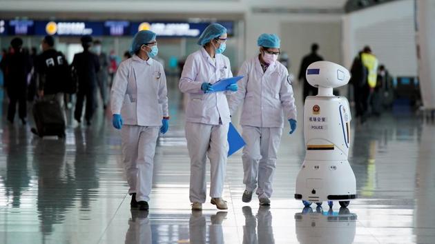 Medical workers walk by a police robot after travel restrictions to leave Wuhan. (REUTERS) Medical workers walk by a police robot after travel restrictions to leave Wuhan. (REUTERS)