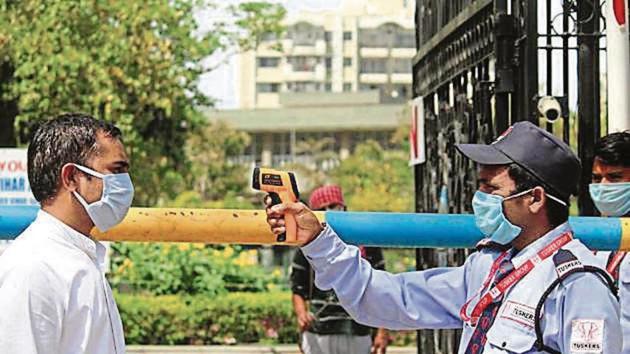 A security guard checks the temperature of a resident of Devinder Vihar.