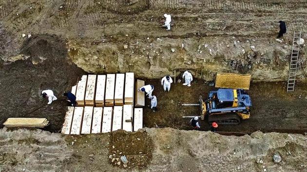 Workers wearing protective equipment bury bodies in a trench on Hart Island on Thursday in the Bronx borough of New York as the death toll in the state continued to mount, putting health care and funeral infrastructure under stress.(Photo: AP)