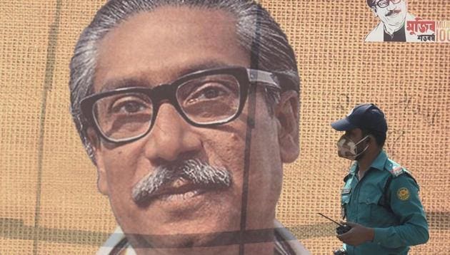 In this file photo taken on March 9, 2020 a policeman wearing a facemask amid fears of the spread of COVID-19 novel coronavirus, walks past a banner with a picture of Bangladesh’s founder Sheikh Mujibur Rahman in Dhaka.(AFP File)