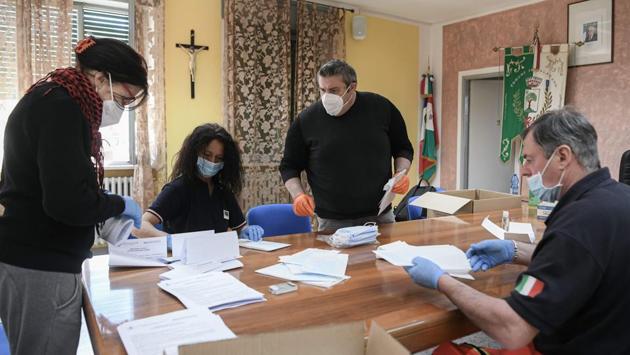 Mayor Fabio Braglia (third from left), who has organised the home visits by AVAP, has also found volunteers to prepare envelopes stuffed with protective masks, which are later delivered to each Palagano resident by the local police. (Piero Cruciatti / AFP) Mayor Fabio Braglia (third from left), who has organised the home visits by AVAP, has also found volunteers to prepare envelopes stuffed with protective masks, which are later delivered to each Palagano resident by the local police. (Piero Cruciatti / AFP)