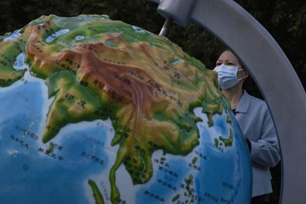 A woman wearing a mask against the coronavirus looks at a globe showing China in Wuhan in central China's Hubei province.(AP)