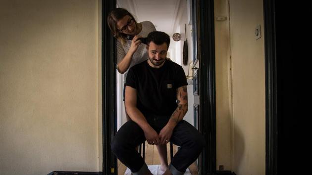 Lucie cuts the hair of her companion Pierre as he faces issues with his haircut like many people during lockdown, in front of the door of their apartment in Paris. There are as many ways of experiencing confinement as there are people. (Elena Fusco / AFP)