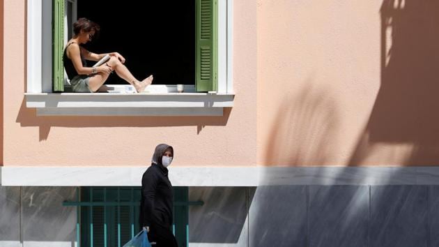 A woman reads as she sits in a window as another woman carries bags after shopping at an open market following the coronavirus disease outbreak (Covid-19) ahead of Greek Orthodox Easter in Athens, Greece, April 17, 2020.(Reuters photo)