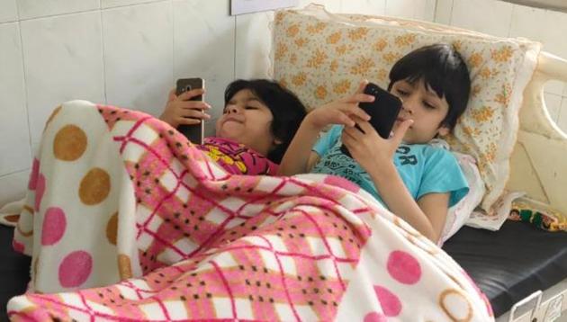 Eight-year-old Arush (right) and his sister Aaina, 6, playing games on mobile phones during their time in the isolation ward of Sirsa civil hospital.(SOURCED)