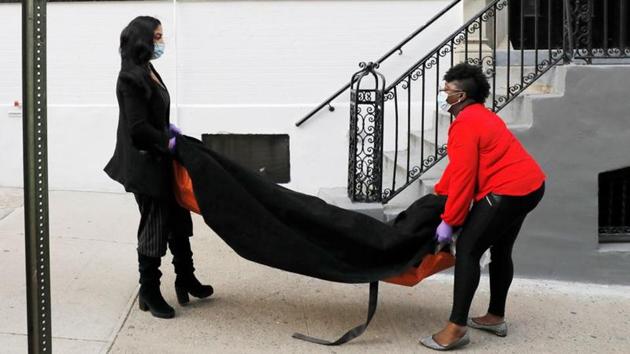 Alisha Narvaez, the manager and Nicole Warring, a Resident Funeral Director carry a deceased person into the basement area, where bodies are stored and prepared for funeral services, during the coronavirus (COVID-19) outbreak, in Manhattan, New York City. (Andrew Kelly / REUTERS) Alisha Narvaez, the manager and Nicole Warring, a Resident Funeral Director carry a deceased person into the basement area, where bodies are stored and prepared for funeral services, during the coronavirus (COVID-19) outbreak, in Manhattan, New York City. (Andrew Kelly / REUTERS)