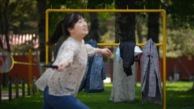 A pair of face masks hang on a coat rack with other items of clothing as a student in the foreground plays badminton at a park in Beijing. (Wang Zhao / AFP)