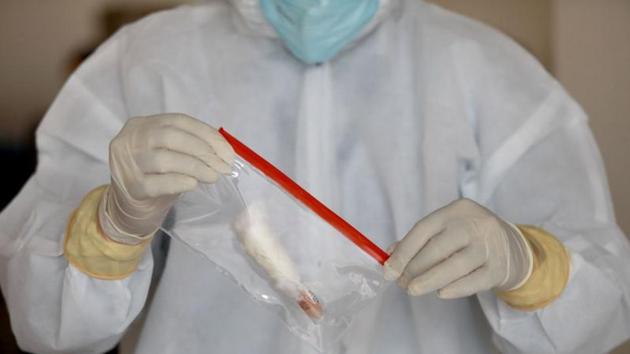 A doctor wearing a protective suit seals a bag containing a swab sample vial, at a testing center for Covid-19 in New Delhi.(REUTERS)