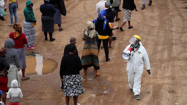 A man in protective clothing speaks trough a loudspeaker as he addresses locals queueing ahead of food distribution amid the spread of the coronavirus disease, in South Africa on April 28.(Reuters Photo)