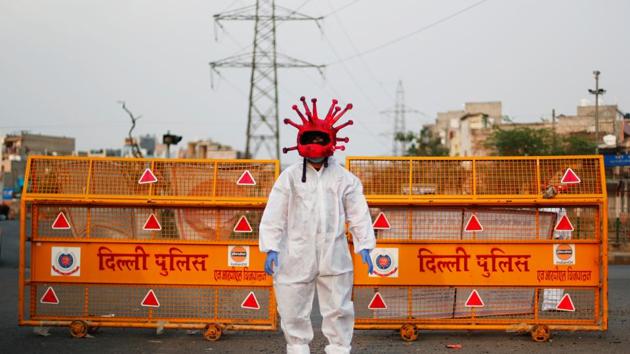 An artist wearing a coronavirus-shaped helmet and a protective suit stands next to a police barricade as he requests people to stay at home during an extended lockdown to slow the spread of the coronavirus disease (Covid-19) in New Delhi.(REUTERS)