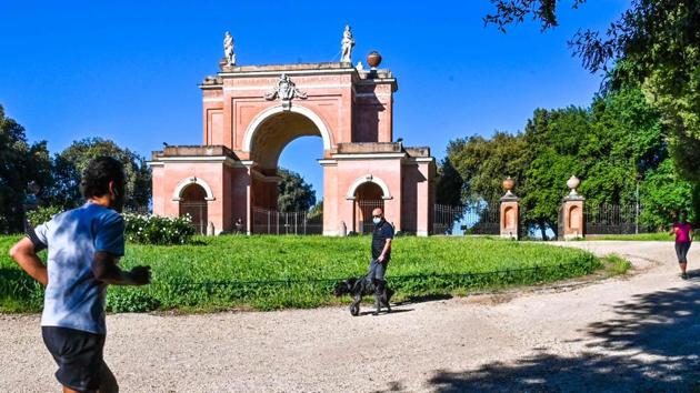 A man jogs while another walks his dog in the park of the Villa Doria Pamphili in Rome. Italy has reported 209,328 cases and 28,710 deaths until now. On May 4, after eight weeks of lockdown – Italy allowed its citizens to exercise outdoors and visit relatives, given proper adherence of social distancing norms and wearing facemasks were followed. Museums and libraries are scheduled on open on May 18. (Andreas Solaro / AFP) A man jogs while another walks his dog in the park of the Villa Doria Pamphili in Rome. Italy has reported 209,328 cases and 28,710 deaths until now. On May 4, after eight weeks of lockdown – Italy allowed its citizens to exercise outdoors and visit relatives, given proper adherence of social distancing norms and wearing facemasks were followed. Museums and libraries are scheduled on open on May 18. (Andreas Solaro / AFP)