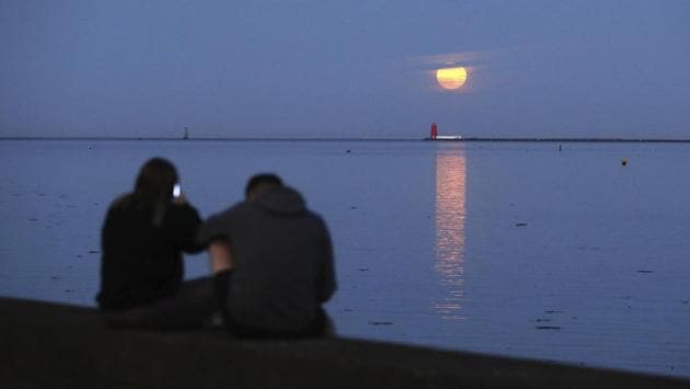 A couple watch as the final supermoon of the year rises over Poolbeg Lighthouse in Dublin Bay, Ireland on May 7. From Japan to Caracas, locals donning masks ventured out to take photos of the celestial spectacle. (Brian Lawless / PA via AP) A couple watch as the final supermoon of the year rises over Poolbeg Lighthouse in Dublin Bay, Ireland on May 7. From Japan to Caracas, locals donning masks ventured out to take photos of the celestial spectacle. (Brian Lawless / PA via AP)