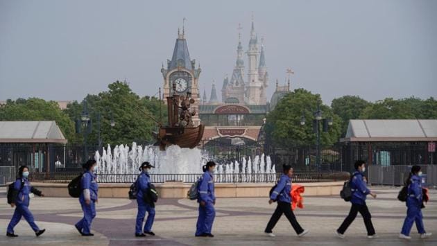 The Shanghai Disneyland Park is seen in the background as park staff walks in a line while maintaining social distance. The reopening of the park is one of the largest test cases yet of whether mass gatherings can take place safely amid the virus pandemic (Aly Song / REUTERS)