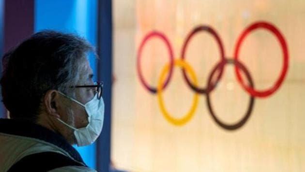 A man wearing a protective face mask, following an outbreak of the coronavirus, stands in front of The Tokyo Olympic flag 1964 at The Japan Olympics museum in Tokyo.(REUTERS)