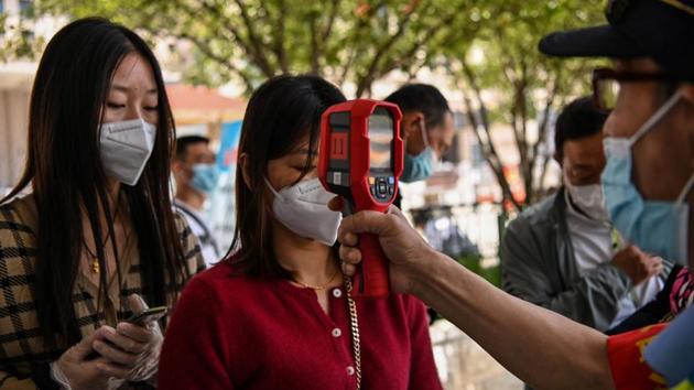 A worker wearing a face mask thermal-scans passengers before they take a taxi after arriving at Hankou railway station, in Wuhan. The central Chinese city of Wuhan where the coronavirus first emerged late last year will test all its citizens for the virus after six new cases were reported over the weekend for the first time since early April. (Hector RETAMAL / AFP)