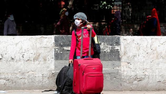 A girl wearing a face mask and a protective cap waits with her belongings outside a railway station in New Delhi, India.(REUTERS)