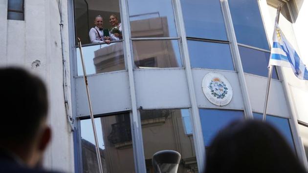 Newlyweds Jenny Gutierrez (L) and Eduardo Camacho look outside to friends and family on the street after getting married at a civil status registration office amid the coronavirus outbreak in Uruguay. A month ago, a glamorous wedding celebration in the Carrasco neighbourhood became a hotspot after it emerged that 44 guests contracted the coronavirus at the wedding. (Mariana Greif / REUTERS)