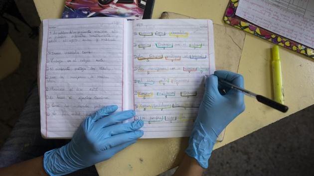 A teacher wearing surgical gloves as a precaution against the coronavirus, corrects a student’s homework at the “Fe y Alegria,” or Faith and Happiness school in Caracas. The children’s homework is brought to the school by their parents who do not have access to the internet, making it impossible for their children to receive online instruction. (Ariana Cubillos / AP) A teacher wearing surgical gloves as a precaution against the coronavirus, corrects a student’s homework at the “Fe y Alegria,” or Faith and Happiness school in Caracas. The children’s homework is brought to the school by their parents who do not have access to the internet, making it impossible for their children to receive online instruction. (Ariana Cubillos / AP)
