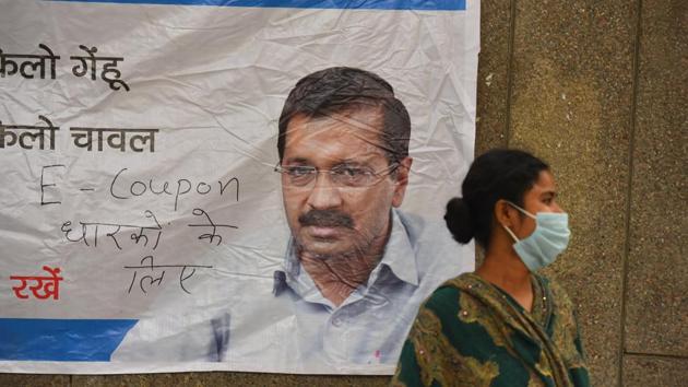 A woman wearing facemask seen next to a poster of Delhi Chief Minister Arvind Kejriwal during a community feeding session at New Ashok Nagar, in New Delhi.(Raj K Raj/HT PHOTO)