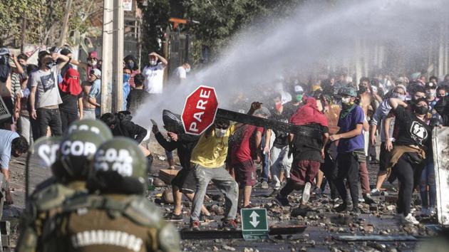 Demonstrators take cover after water cannons were launched at them. The municipality said in a statement that families were going hungry in the poorest sectors of El Bosque, a neighbourhood where many work informally, or not at all -- reported Reuters. (AP / PTI)