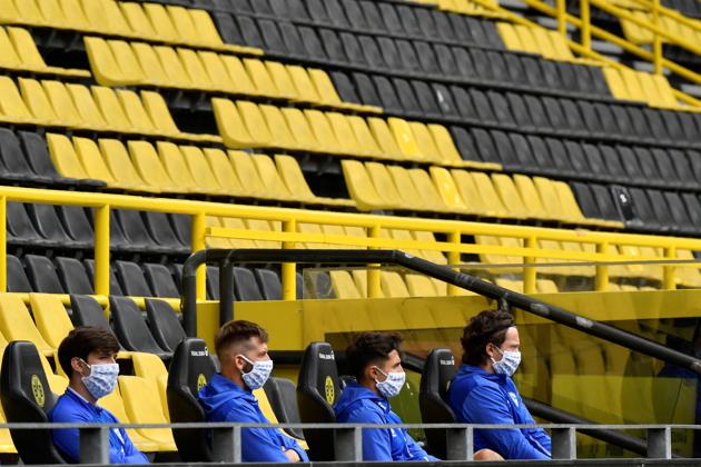 Substitutes wearing protective face masks maintain social distance, as play resumes behind closed doors following the outbreak of the coronavirus disease. (REUTERS)