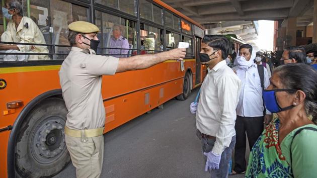 A policeman thermal screens people before they board a bus in Delhi on May 19. All public modes of transport, with the exception of the Delhi Metro, are now operating in Delhi with applicable restrictions. Private cars are allowed, but with a maximum of two passengers and a driver. Pillion riding is not permitted on two-wheelers. (Prateek Kumar / ANI)