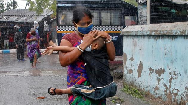 A woman in Kolkata carries her son as she tries to protect him from heavy rain while they rush to a safer place, following their evacuation from a slum area just before Cyclone Amphan made its landfall in West Bengal this afternoon. At 3:05 pm, the wind speed at Kolkata airport was recorded at 76 km per hour, the meteorological office told HT. (Rupak De Chowdhuri / REUTERS)