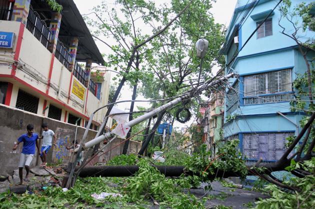 People walk past a damaged electrical pole on a road, in the aftermath of super cyclone 'Amphan', in Kolkata. (PTI Photo) People walk past a damaged electrical pole on a road, in the aftermath of super cyclone 'Amphan', in Kolkata. (PTI Photo)
