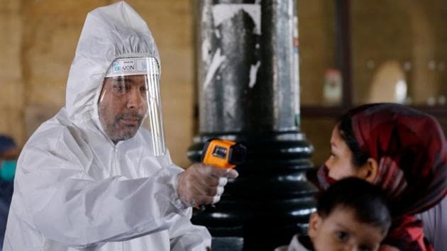 A railway worker wearing a protective gear measures the temperature of a passenger before she boards a train to her hometown, in Karachi on Wednesday.(Reuters Photo) A railway worker wearing a protective gear measures the temperature of a passenger before she boards a train to her hometown, in Karachi on Wednesday.(Reuters Photo)