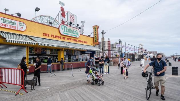 Pedestrians wearing protective masks walk past Nathan’s Famous Inc. restaurant on the Coney Island boardwalk in New York. Without clear federal guidance, state and local officials have been left to figure out how to celebrate the holiday safely. (Jeenah Moon/Bloomberg)