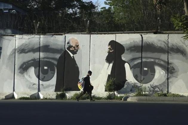 A young boy carries a sack of goods on his back as he walks past a wall depicting Washington's peace envoy Zalmay Khalilzad and Mullah Abdul Ghani Baradar, the leader of the Taliban delegation, Kabul, Afghanistan, Tuesday, May 4, 2020(AP)