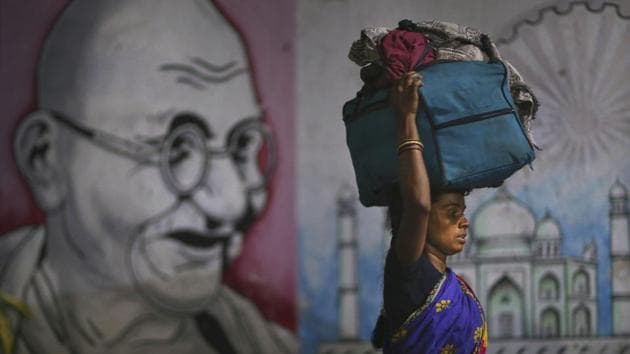 A migrant woman carries her belongings on her head as she walks past a wall painting of Mahatma Gandhi to board a train to her home state. (AP) A migrant woman carries her belongings on her head as she walks past a wall painting of Mahatma Gandhi to board a train to her home state. (AP)