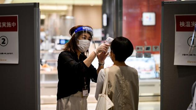 An employee wearing a mask and face shield conducts a temperature check on a customer at the entrance of the Shibuya Hikarie building in Tokyo on May 26. Unlike strict lockdowns in other countries, Japan did not force businesses to close. (Behrouz Mehri / AFP) An employee wearing a mask and face shield conducts a temperature check on a customer at the entrance of the Shibuya Hikarie building in Tokyo on May 26. Unlike strict lockdowns in other countries, Japan did not force businesses to close. (Behrouz Mehri / AFP)