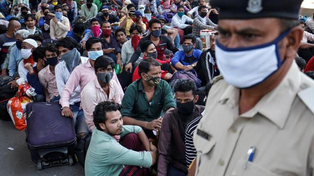 A police officer stands guard as migrant workers and their families wait to get on a bus to reach a railway station to board a train to their home state of Bihar, during an extended lockdown to slow the spreading of the coronavirus disease (Covid-19). (REUTERS) A police officer stands guard as migrant workers and their families wait to get on a bus to reach a railway station to board a train to their home state of Bihar, during an extended lockdown to slow the spreading of the coronavirus disease (Covid-19). (REUTERS)