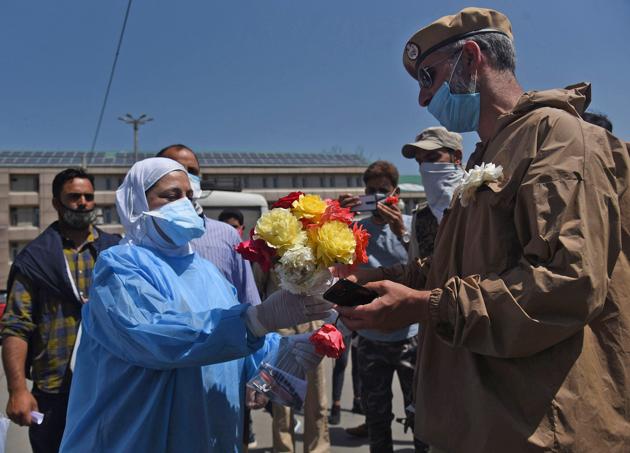 A cop offering flowers to a doctor outside LD Hospital in Srinagar following outrage over reports of harassment of doctors by policemen amid Covid-19 lockdown.(Waseem Andrabi/HT)