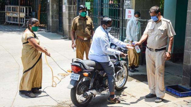 A staff member arriving at the Katraj zoo is dispensed sanitizer while police personnel sanitize his motorbike. The lockdown due to the coronavirus has brought about an abrupt fall in the number of visitors and revenue. The zoo has been closed to the public since March 14. (Milind Saurkar / HT Photo)