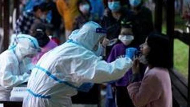 A medical worker in a protective suit conducts a nucleic acid testing for a resident as people wearing masks queue behind for testings, at a residential compound in Wuhan, the Chinese city hit hardest by the coronavirus disease.(REUTERS)