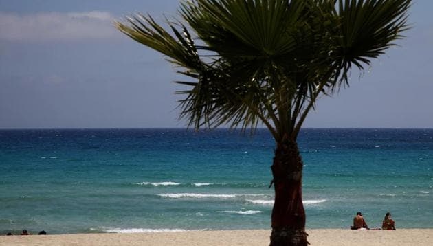 FILE - In this file image taken on Sunday, May 10 2020, sunbathers sit on an empty stretch of 'Landa' beach at the Cyprus seaside resort of Ayia Napa, a favorite among tourists. Cyprus' government Wednesday May 27, 2020, is pledging to cover all costs for anyone testing positive for the coronavirus while on vacation in the east Mediterranean island nation, covering the costs of lodging, food, drink and medication for COVID-19 patients and their families.(AP Photo/Petros Karadjias, FILE)(AP)