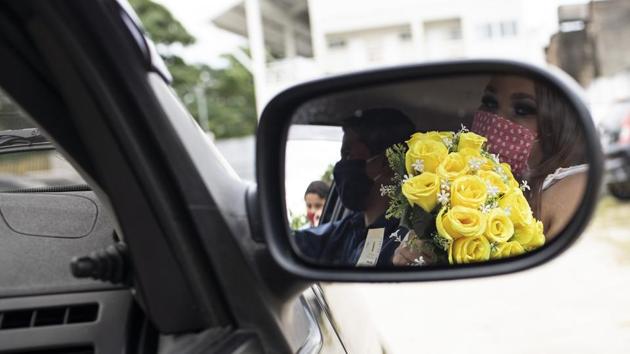 A bride is reflected on a car rear view window as she holds her bouquet after her drive-thru wedding. “We’re very happy because we didn’t think we wedding date would come so soon,” Erica Blank told AP. “We found out a week ago that we would get married and it was so good,” Blank adds. (Silvia Izquierdo / AP)