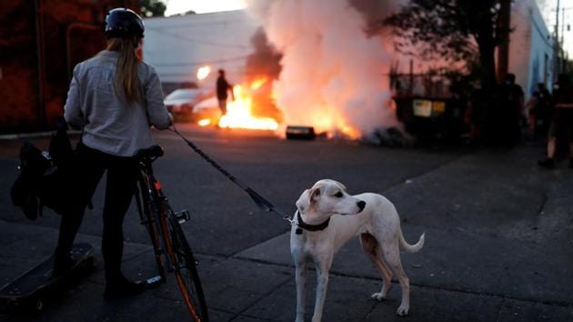 A woman holding a dog looks on burning cars during a demonstration in Minneapolis, Minnesota on May 29. (Carlos Barria / REUTERS) A woman holding a dog looks on burning cars during a demonstration in Minneapolis, Minnesota on May 29. (Carlos Barria / REUTERS)