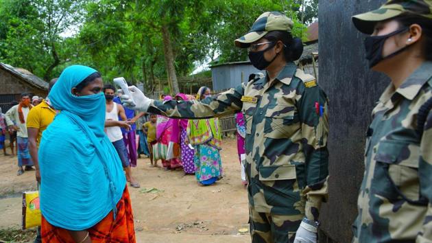 A personnel doing a thermal check of a woman as people in India-Bangladesh border are waiting to get their ration in the fencing, during the nationwide lockdown near Motinagar area, in Agartala on Friday.(ANI photo)