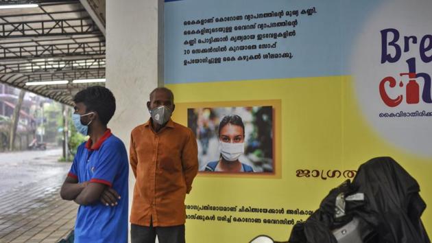 Indians wearing masks stand next to a signage that urges people to wash their hands and wear masks to protect against the COVID-19 pandemic in Kerala.(AP)